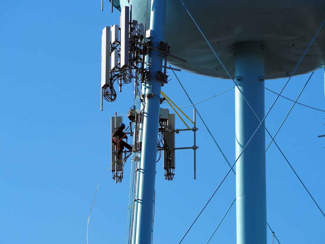 A maintenance worker, dozens of feet above the ground, works on cell phone antennas attached to the legs of a water tower in Sanatoga PA during January 2025.